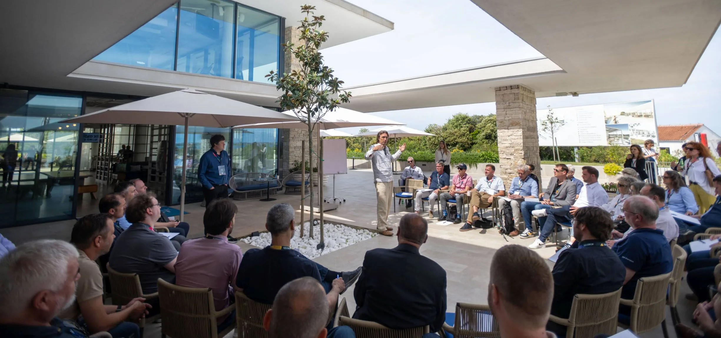 Attendees seated in a circle around a speaker at a workshop on a sunny terrace